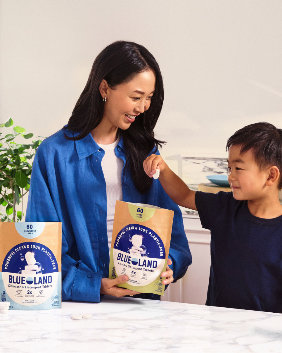 Woman and child holding Blue Land laundry detergent packages in a kitchen.