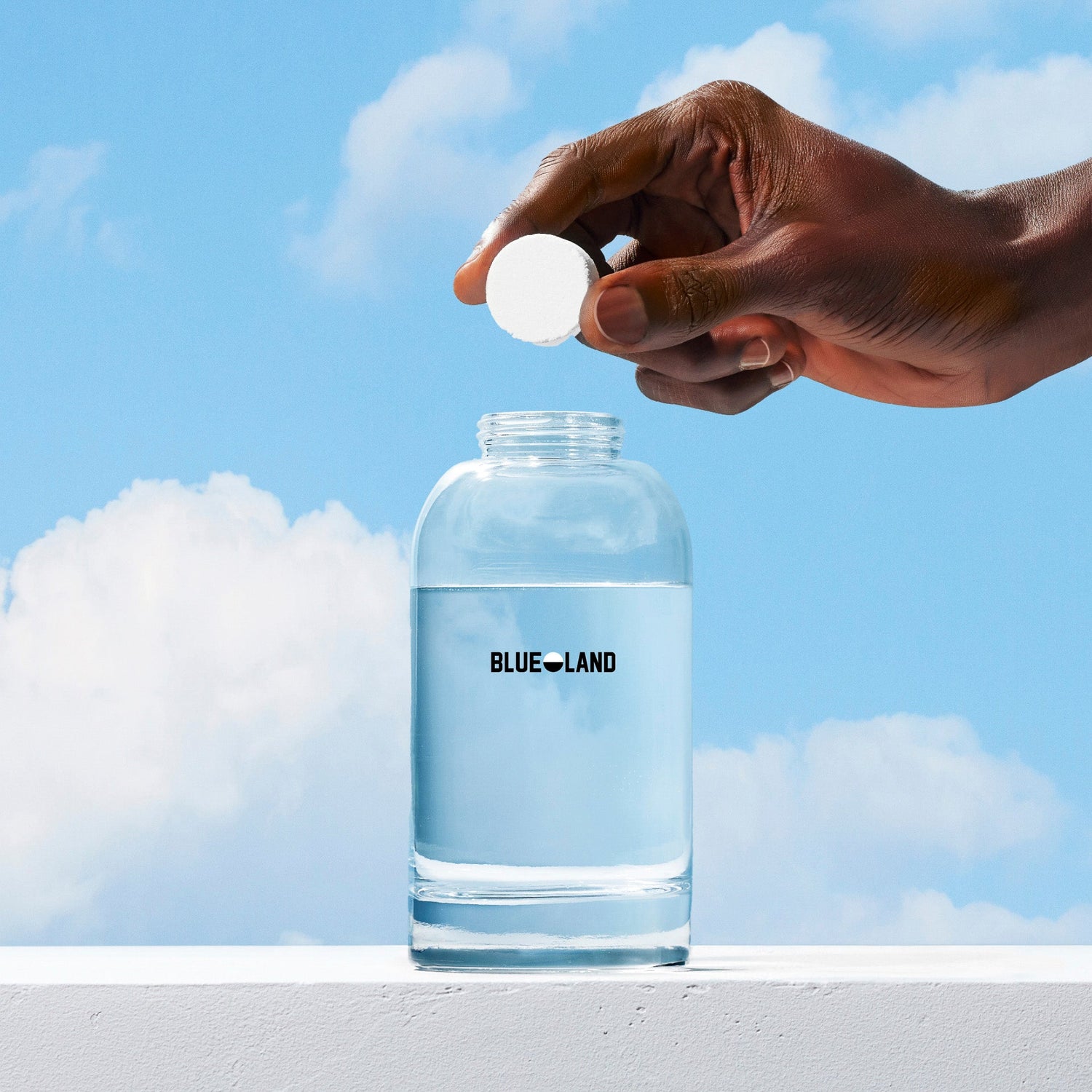 Hand holding a white tablet above a Blue Land water bottle with a blue sky background