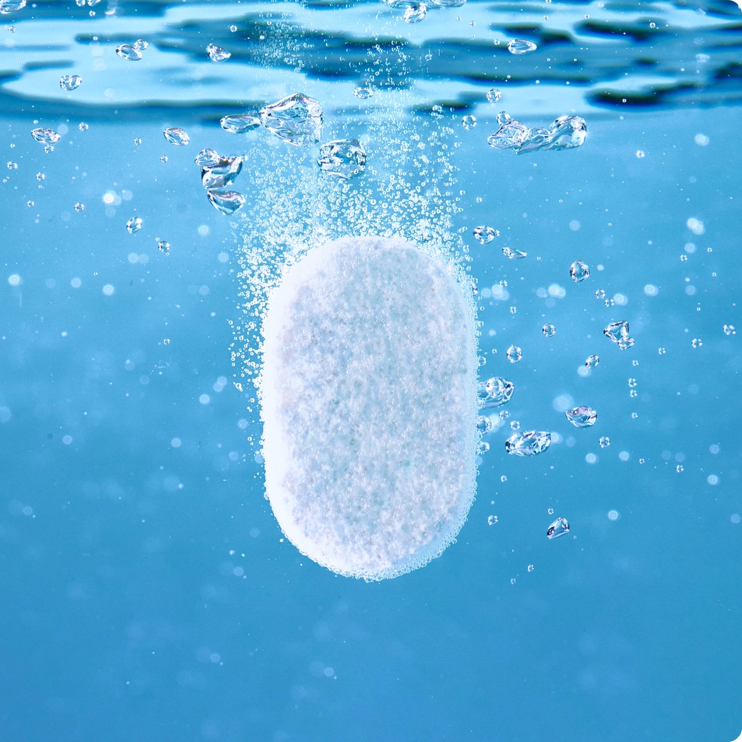 A white tablet is dissolving underwater, releasing bubbles and creating a fizzy effect against a blue background.